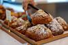 A pair of tongs picking up an almond croissant from a pile