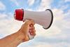 A megaphone being held by a white person's hand against a blue sky