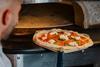 Chef Marco Greco puts a freshly prepared pizza into an oven.  2100x1400