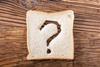 A slice of white bread, with a question mark cut out of it, on a wooden table