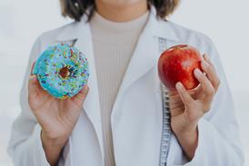 A person holding a blue sprinkled doughnut in one hand, and an apple in the other