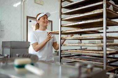 A young female baker putting sausage rolls onto a tray
