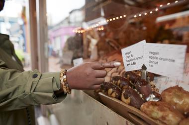 A person pointing at a vegan chocolate & hazelnut doughnut in a bakery window