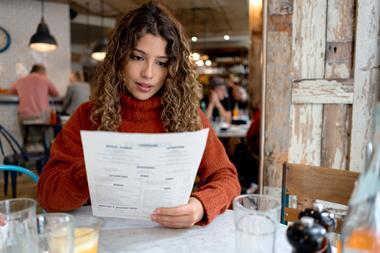 A woman in a red jumper looking at a menu in a nice restaurant