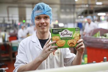 An employee holds up a box of Mr Kipling Bramley Apple pies at a production site.  2100x1400