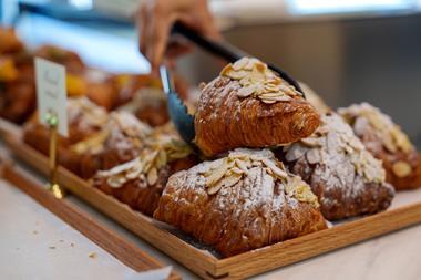 A pair of tongs picking up an almond croissant from a pile