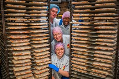 Staff members next to trays of baked pizza