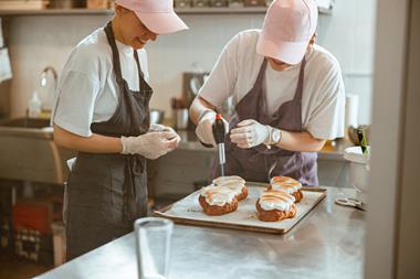 Two young bakers blowtorching meringue on top of a croissant