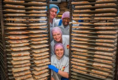 Staff members next to trays of baked pizza