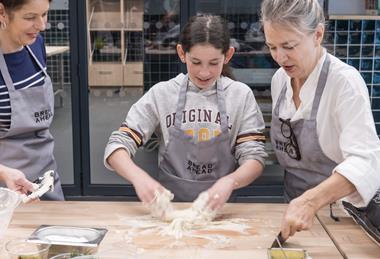 A girl is guided in  dough making by Bread Ahead team members at its baking school in Borough Market, London  2100x1400