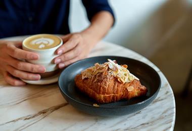 A woman enjoying a cup of coffee and an almond croissant