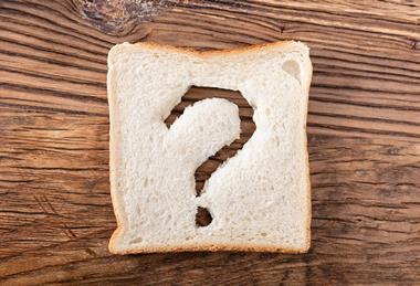 A slice of white bread, with a question mark cut out of it, on a wooden table