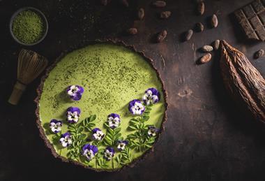 A matcha and chocolate tart with edible purple flowers on top