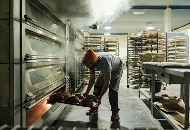 A staff member removes a tray of freshly-baked loaves out of an oven at Company Bakery's existing site in Devon Place, Edinburgh - Company Bakery