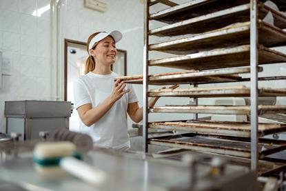 A young female baker putting sausage rolls onto a tray