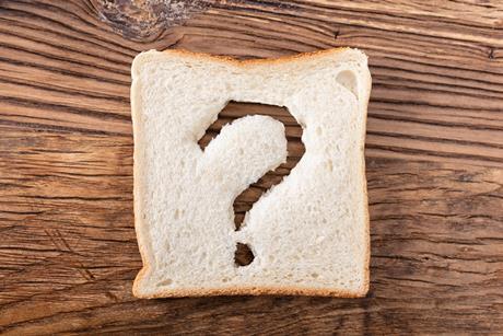 A slice of white bread, with a question mark cut out of it, on a wooden table