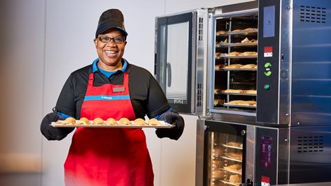 A Greggs colleague holding a tray of sausage rolls on baking paper