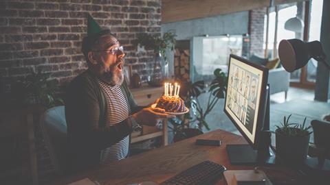 A bearded man blowing out birthday candles in front of a Zoom meeting