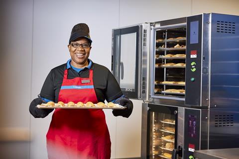 A Greggs colleague holding a tray of sausage rolls on baking paper