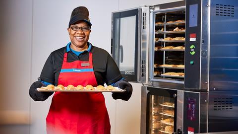 A Greggs colleague holding a tray of sausage rolls on baking paper