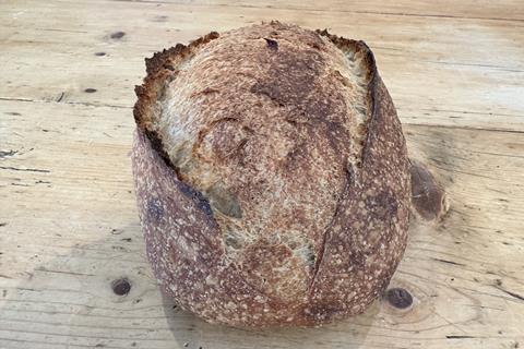A golden brown sourdough loaf on a wooden surface