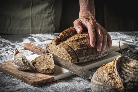 A white male hand holding a sourdough loaf for cutting