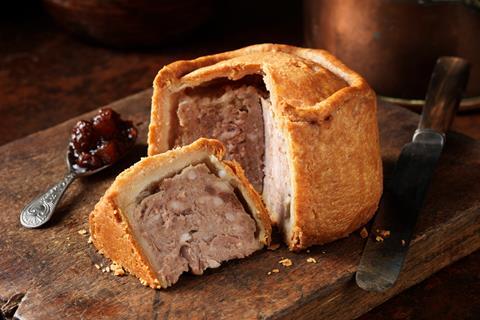 A large pork pie on a chopping board with pickle