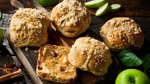 Co-op Apple Crumble Hot Cross Bun with apple and cinnamon sprinkled around it