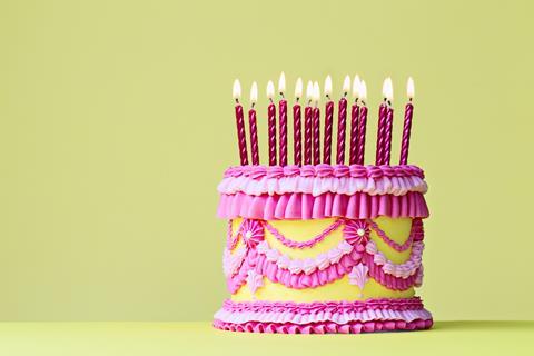 A pink and yellow birthday cake with intricate piped frosting and lots of candles on top