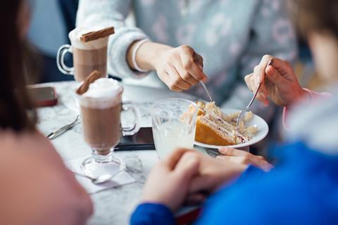 A group of people sharing a slice of cake and hot chocolates