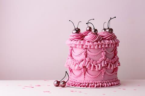 A celebration cake heavily decorated with pink buttercream and topped with cherries