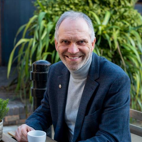 Steve Magnall in a blue blazer smiling at the camera while enjoying a cup of coffee