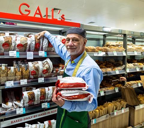 A bearded member of staff in a Waitrose apron stocks sourdough loaves onto a Gail's branded fixture