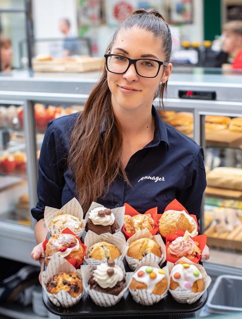 A Bakers + Baristas employee holds a tray of muffins