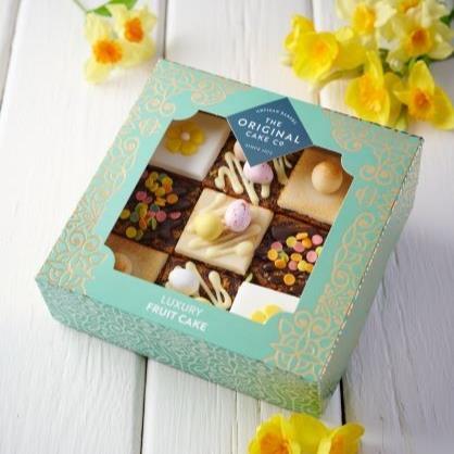 Nine squares of fruit cake with different toppings in an ornate gift box