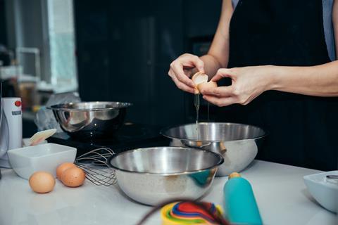 A baker cracks an egg into a mixing bowl.