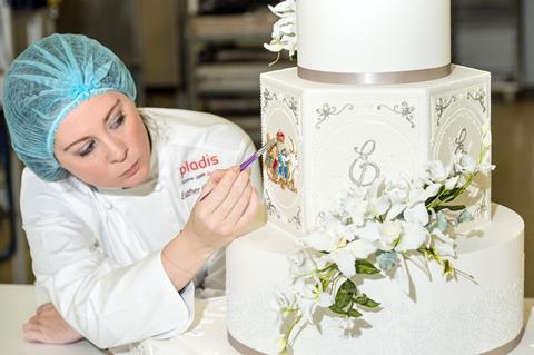 A woman in a hairnet painting details on a wedding cake