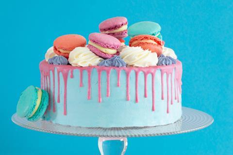 A blue cake with pink drip and topped with macarons and cream