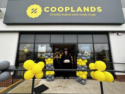 People with a cake and yellow balloons outside a Cooplands Bakery