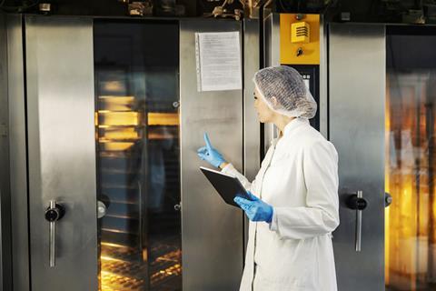 A woman holding an iPad checks bakery products in an industrial oven