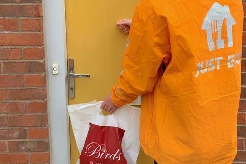 A person in a yellow Just Eat jacket delivering a bag from Birds Bakery