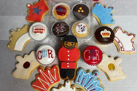 A selection of crown shaped shortbread biscuits with icing on top alongside cupcakes and a gingerbread beefeater