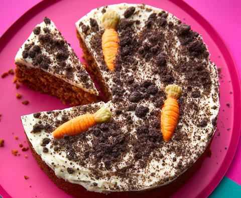 A carrot cake with cream cheese frosting, chocolate carrots and cookie crumb on top