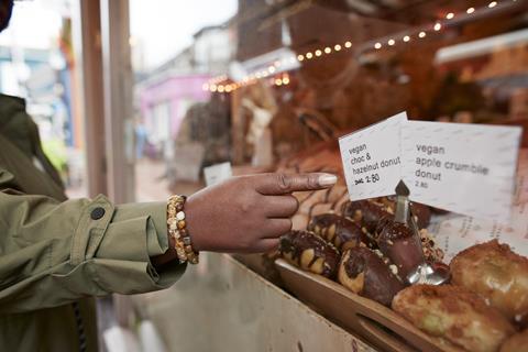 A person pointing at a vegan chocolate & hazelnut doughnut in a bakery window