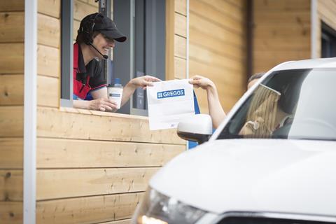 A Greggs staff member hands baked goods to a customer at a drive-thru