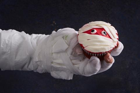 A bandaged 'mummy' hand holding a mummy themed cupcake