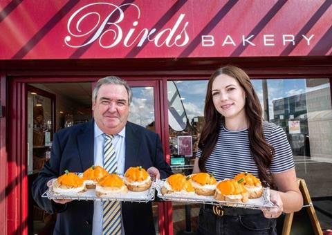 A man and a woman holding pumpkin themed pastries outside of Birds Bakery