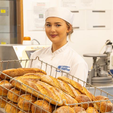 A young female baker holding a tray of freshly baked baguettes