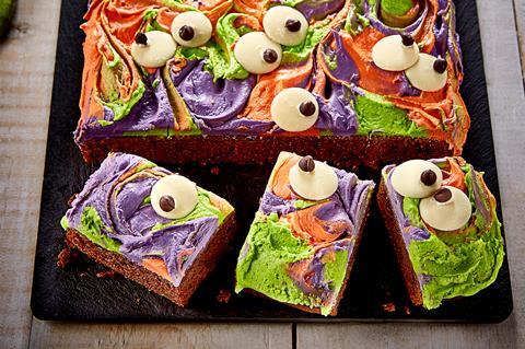 A brownie with swirls of orange, green and purple frosting on top with chocolate eyes