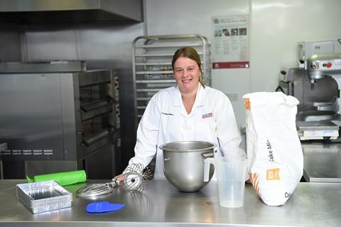 A woman in a white coat with bakery equipment behind her